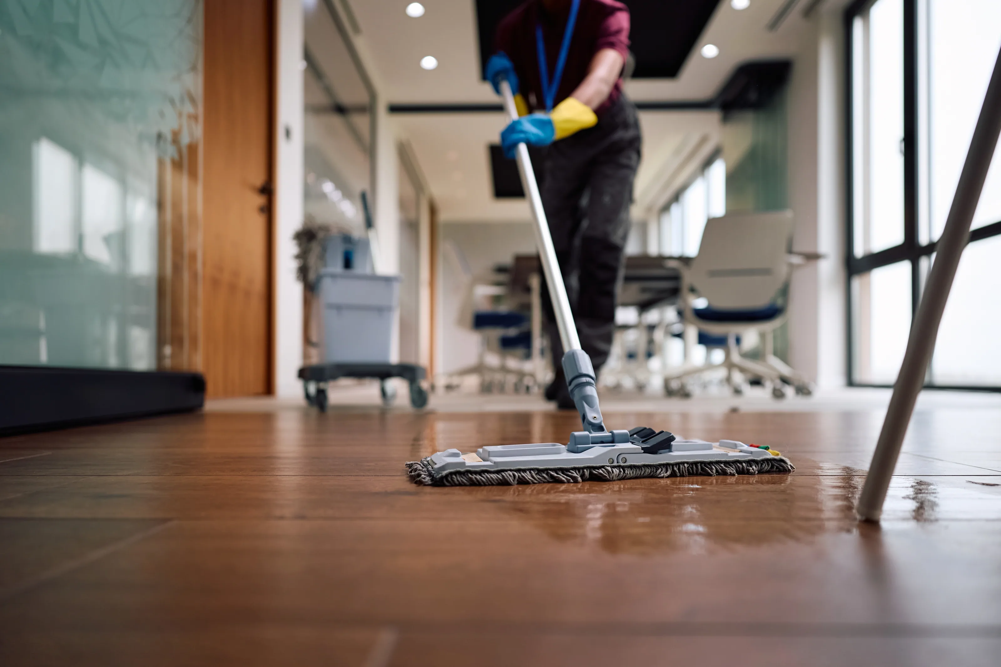 Reinigungskraft wischt den Holzboden eines modernen Büros mit einem Flachmopp